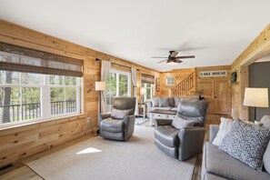 Ein Ferienhaus-Interieur mit einer Couch, Sesseln, einem Deckenventilator und einem Schild mit der Aufschrift 'LAKE HOUSE'.