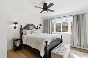 Ein Schlafzimmer mit einem Bett, Nachttischlampen, einem Deckenventilator, einem Fenster mit Vorhängen und einer Bank.
