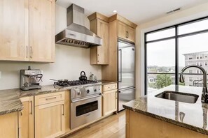 A modern kitchen with a stove, oven, and refrigerator, wooden cabinets, and a large window with a city view. - Luxury DuPont Duplex/Anna Maria Residences 502 (Washington)