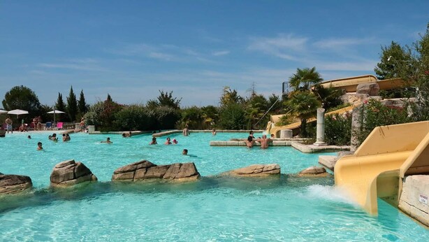Piscina com pedras, toboágua e pessoas nadando.