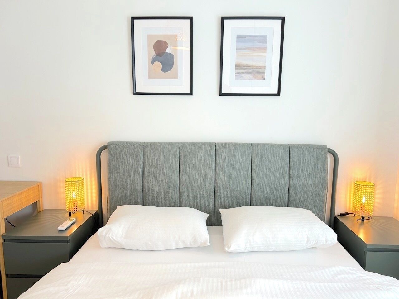 Ein Hotelzimmer mit einem Bett, zwei Nachttischen, einer Lampe und zwei gerahmten Bildern an der Wand.