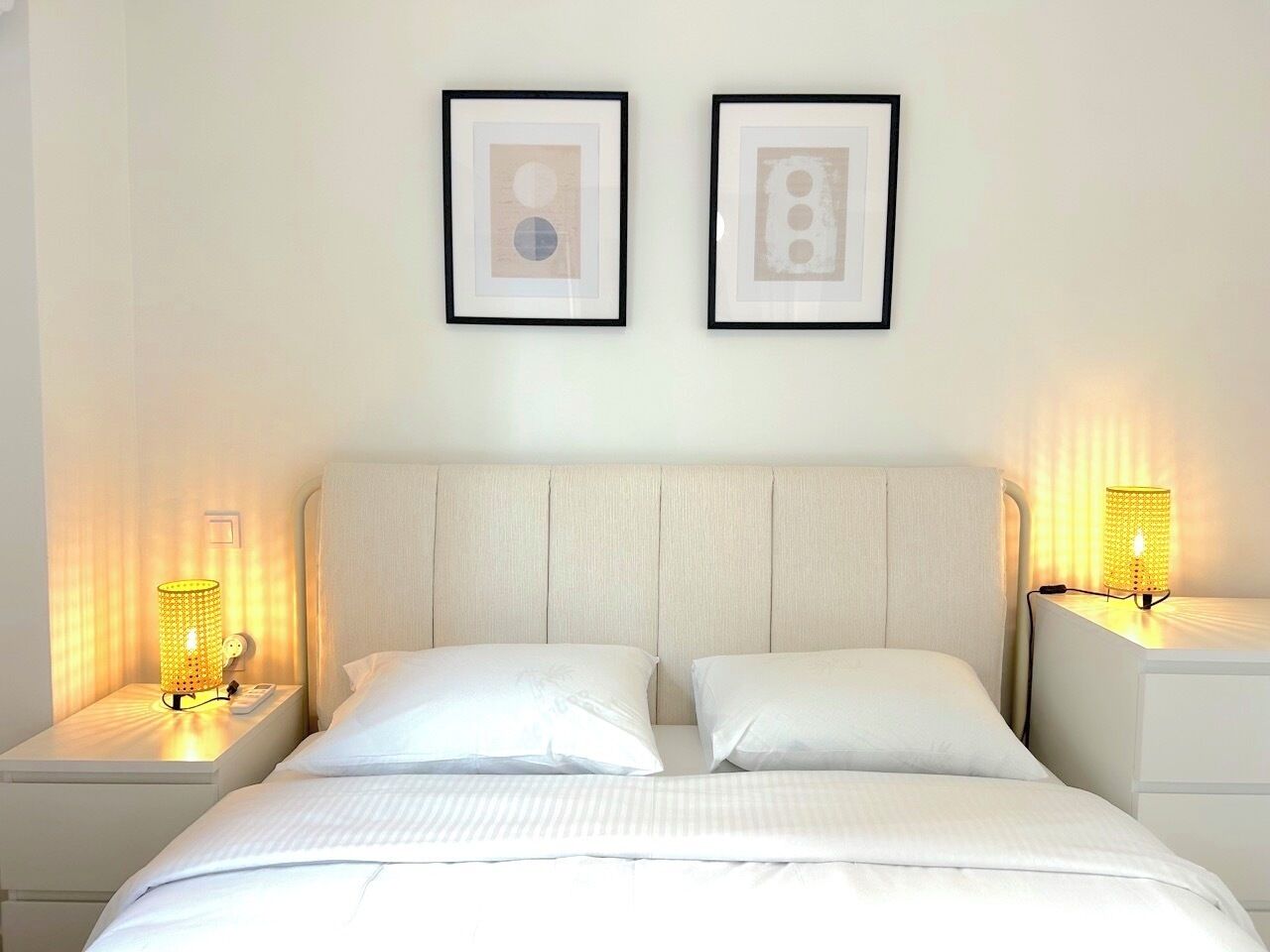 A hotel room with a bed, two bedside tables with lamps, and two framed pictures on the wall.
