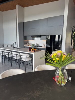 A modern kitchen with grey cabinets, a central island, and a dining area with white chairs.