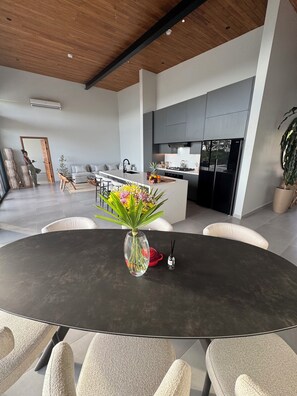 A modern living room with a round table, chairs, a sofa, and a kitchen area with a fridge and stove. - Luxury villa with an ocean view near Playa Venao (Cañas)