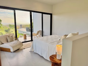 Un dormitorio con una cama grande, un sofá, una mesa y vistas a un jardín a través de una puerta corredera.