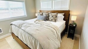 Quarto com cama, mesa de cabeceira, abajur e persianas.
