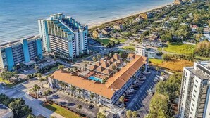 Ett flygbildsfoto av ett hotell vid kusten med en pool, en parkeringsplats och utsikt över stranden.