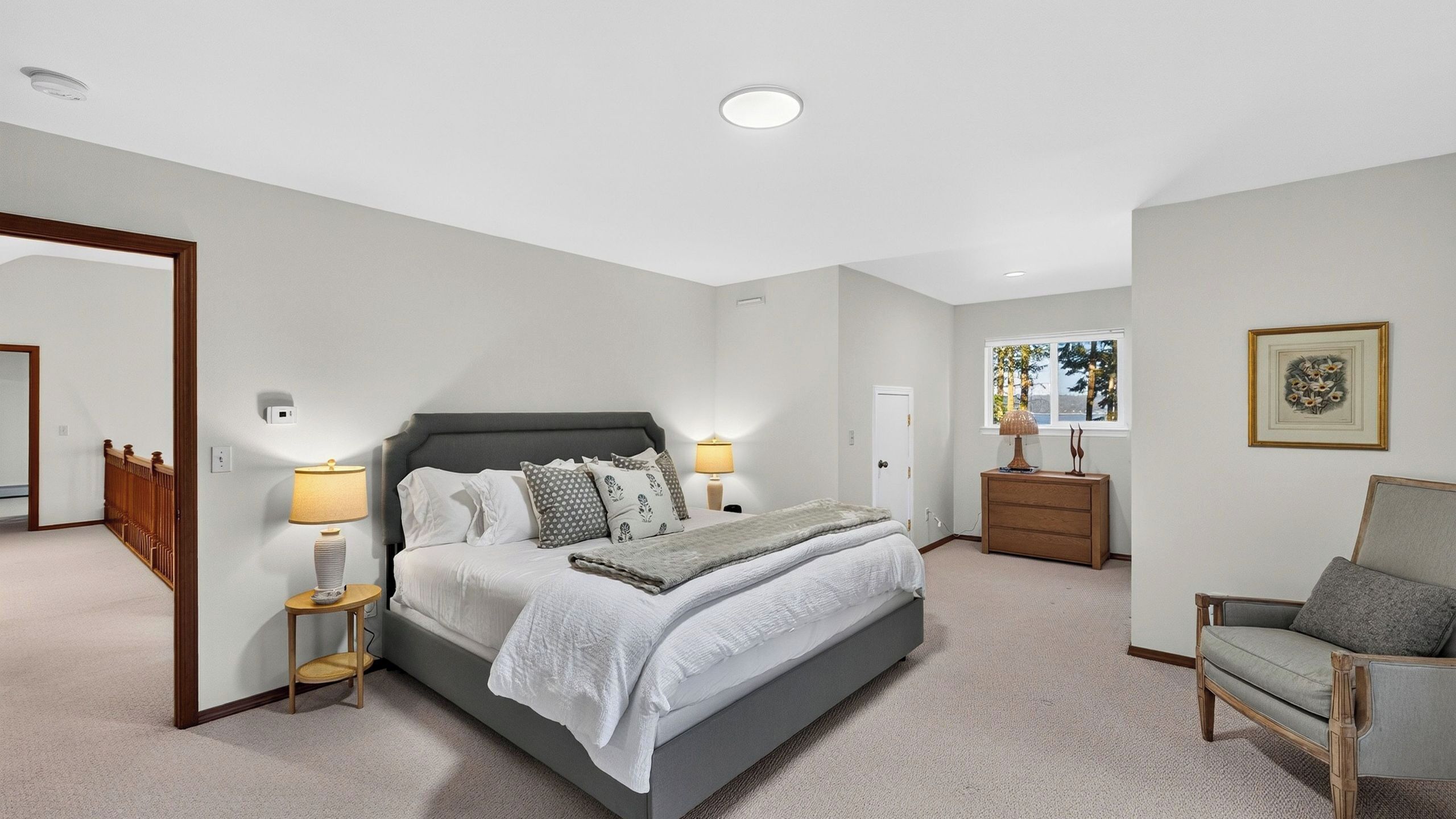 A bedroom with a large bed, bedside lamps, a dresser, a chair, and a window with a view.
