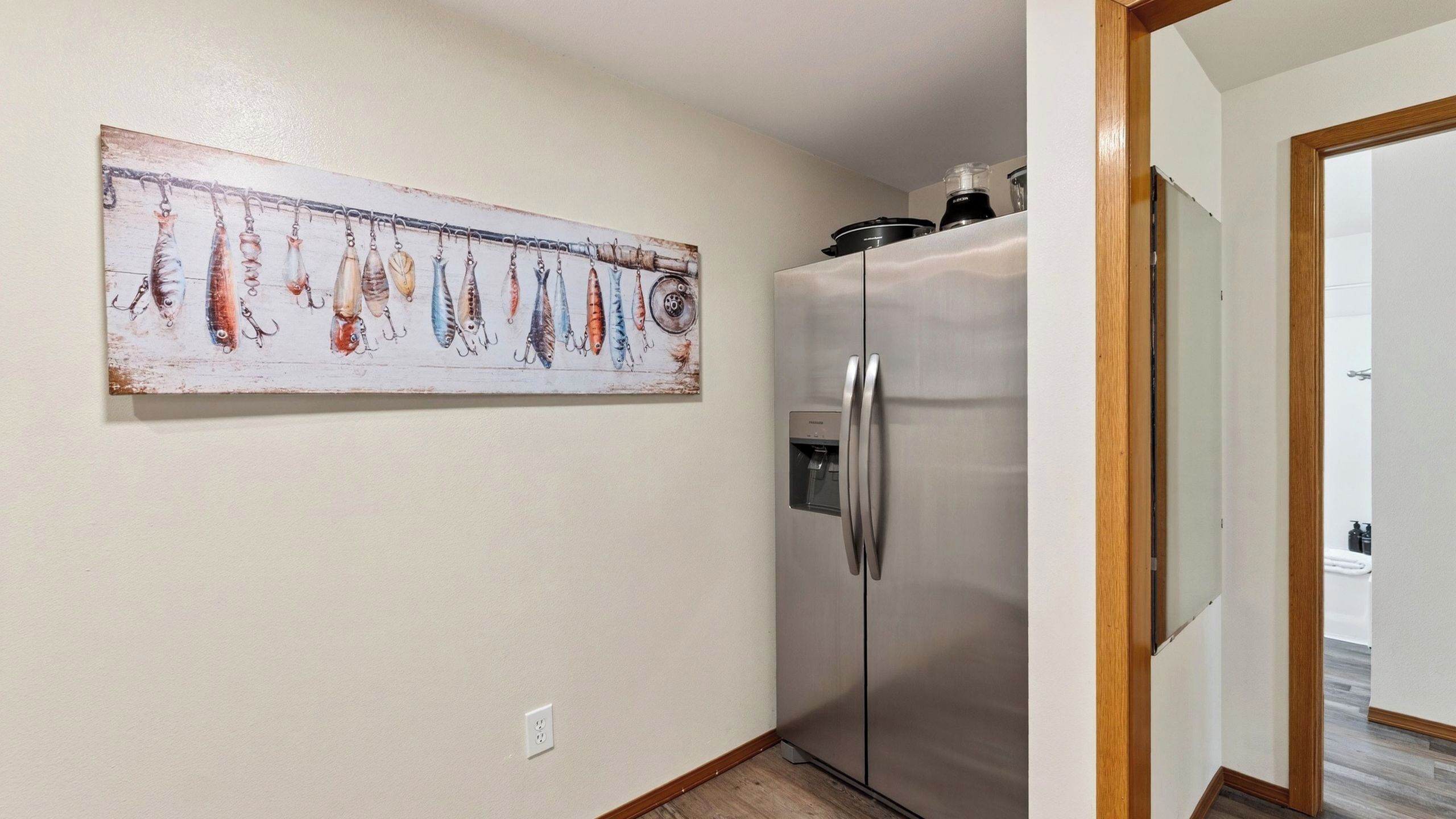 A kitchen with a stainless steel refrigerator, a water dispenser, and a painting of fishing lures on the wall.