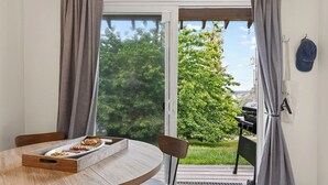 A dining area with a table, chairs, and a tray with food. There is a sliding glass door leading to an outdoor space with a grill and greenery.