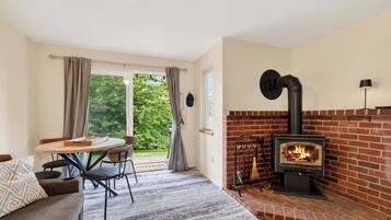 A cozy room with a brick fireplace, a dining table with chairs, and a view of greenery outside.