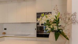 Et moderne køkken med hvide skabe, en hvid bordplade og en vase med hvide blomster.