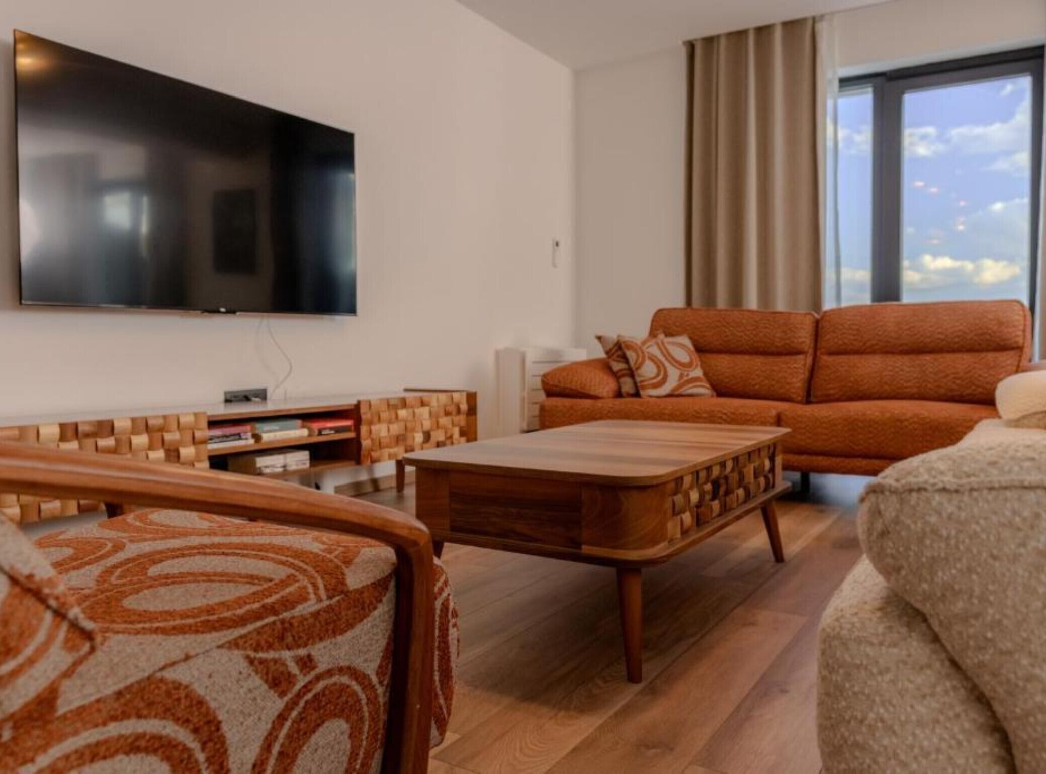 Una sala de estar moderna con un televisor de pantalla plana, un sofá, una mesa de centro y un sillón estampado.
