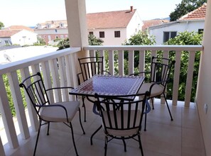 A balcony with a table and chairs, a white railing, and a view of buildings in the background. - One Bedroom Apartment with Balcony ( B ) (Orebic)