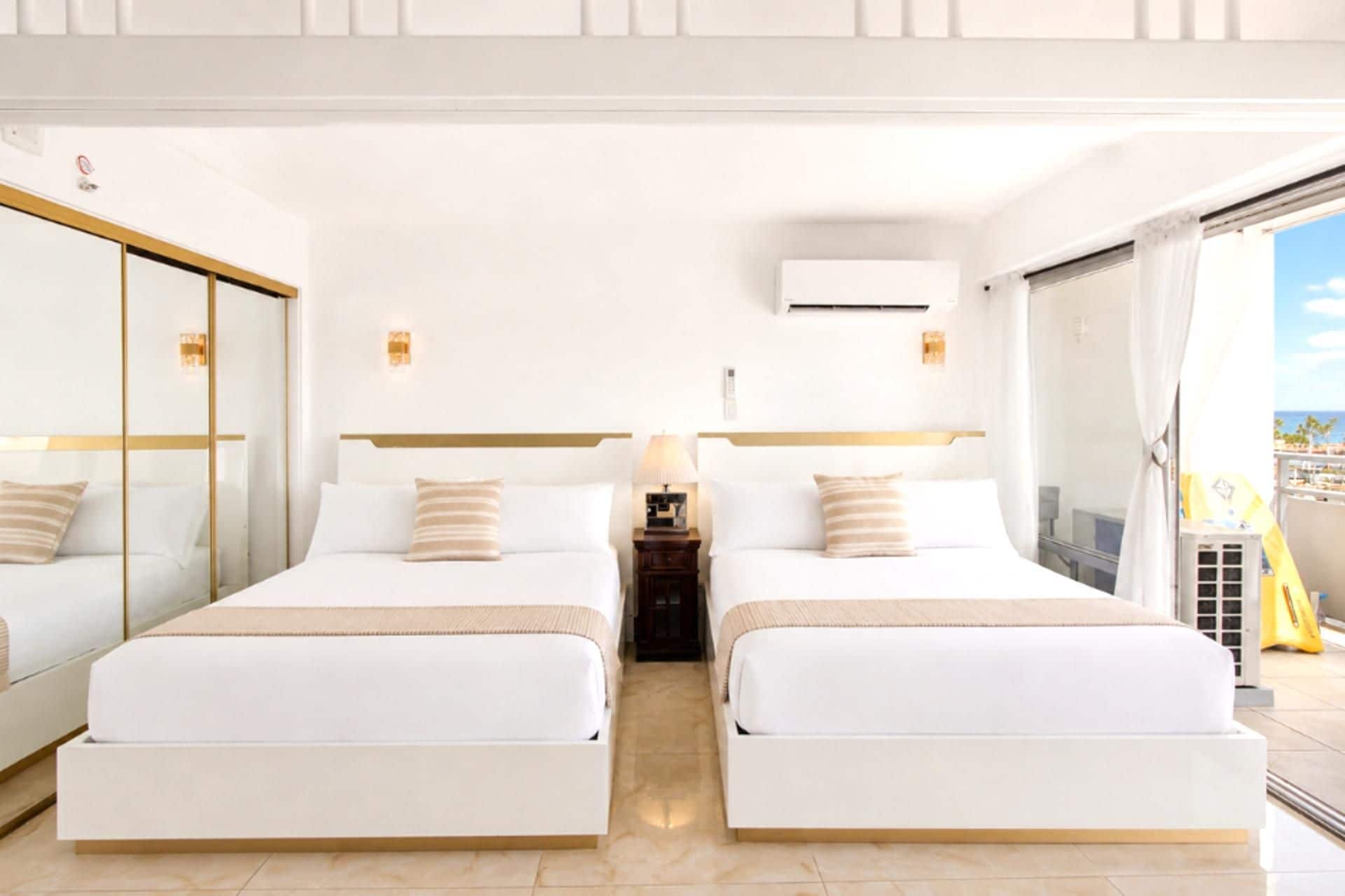 A hotel room with two beds, a large mirror, an air conditioning unit, and a balcony with a view.