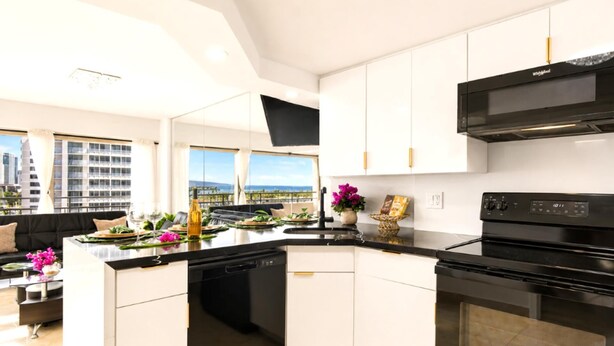 A modern kitchen with a black stove, white cabinets, and a view of the city. - Suite, Ocean View, Studio (Honolulu)