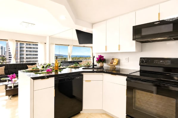 A modern kitchen with a black stove, white cabinets, and a view of the city. - Suite, Ocean View, Studio (Honolulu)