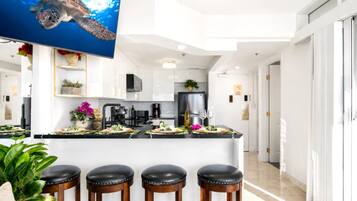 Una cocina moderna con armarios blancos, una isla grande con taburetes, un televisor de pantalla plana y una planta en maceta.