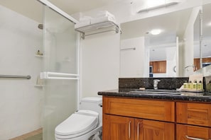 Ein Badezimmer mit Duschkabine aus Glas, Toilette, Holzschränken und einer Ablage mit Toilettenartikeln.