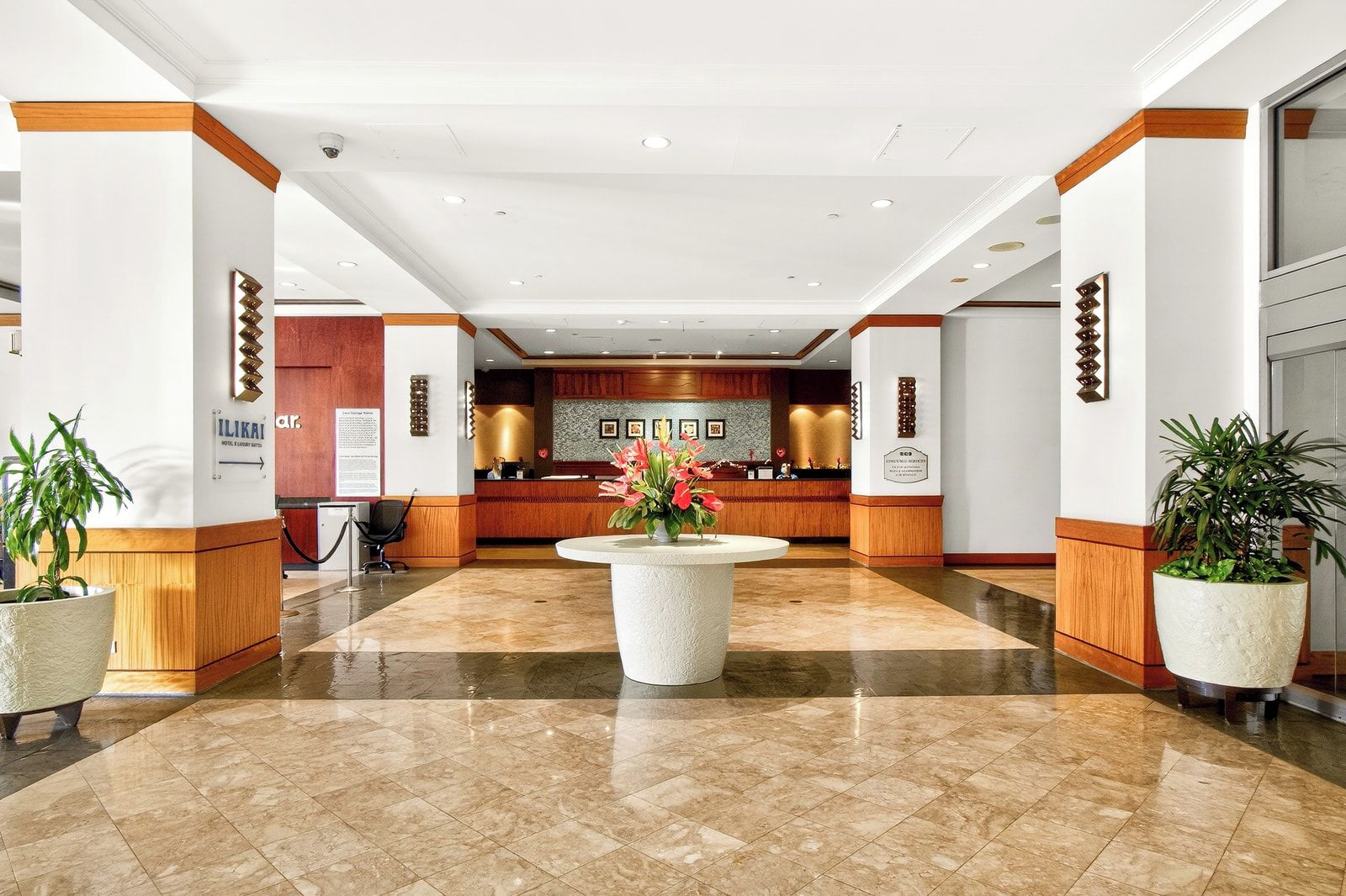 Un vestíbulo de hotel con una recepción, una planta central grande con flores y plantas en macetas.