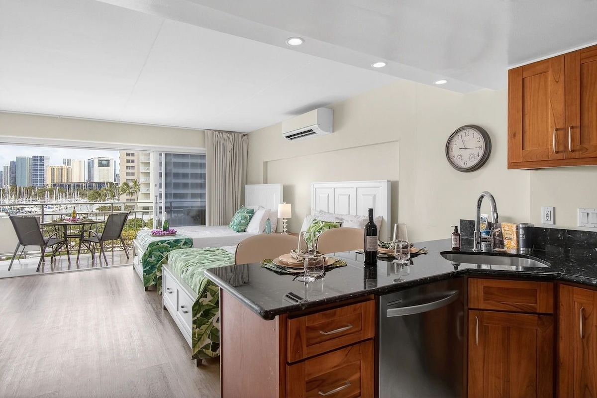 Una habitación de hotel moderna con balcón, comedor y cocina con armarios de madera.