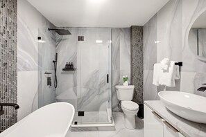 Een moderne badkamer met een douchecabine van glas, een vrijstaand bad, een toilet en een grote wastafel.