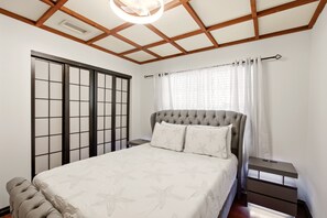 Een slaapkamer met een bed, nachtkastjes, een raam met gordijnen, een plafondventilator en een schuifdeur.