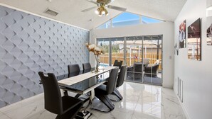 Un comedor moderno con una mesa de vidrio, sillas negras, un ventilador de techo y vistas a través de puertas de cristal amplias.