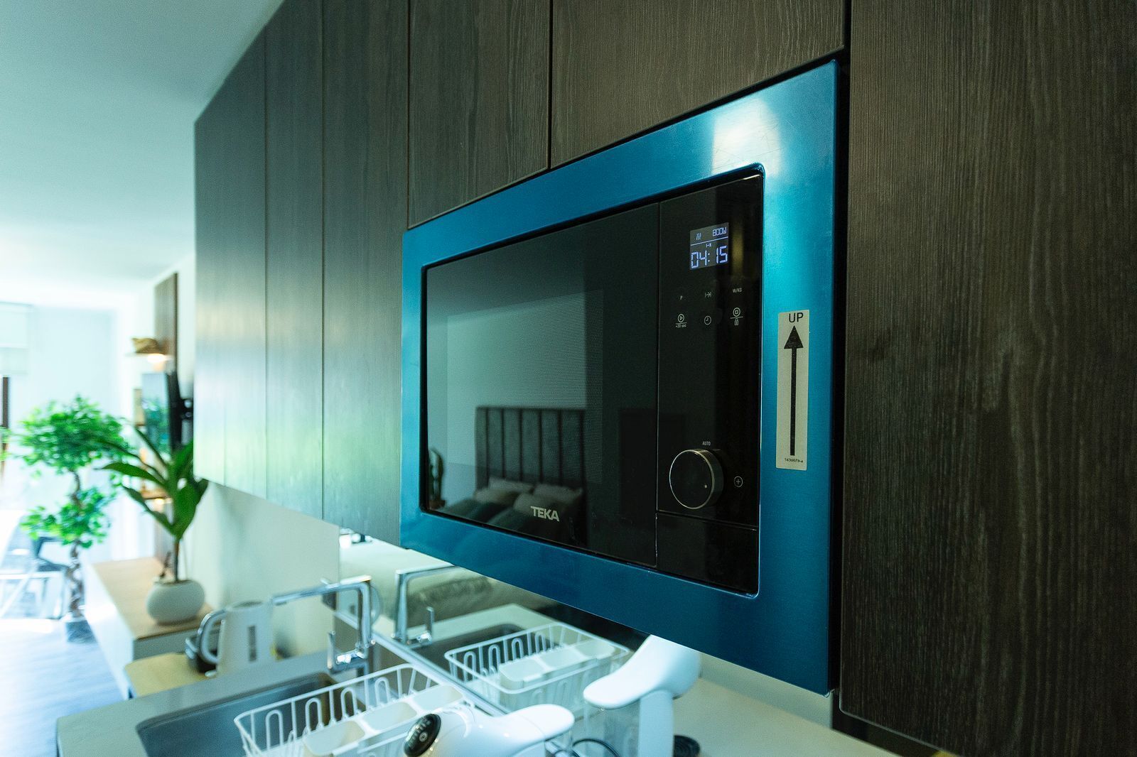 Una cocina moderna con televisión integrada, un lavamanos con escurreplatos y una planta en maceta.