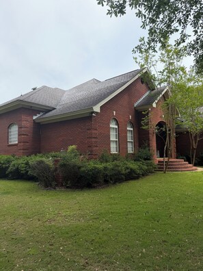 A red brick house with a sloped roof, a front porch, and a well-maintained lawn.