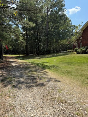 A gravel driveway leading to a grassy area with trees and a building on the right.