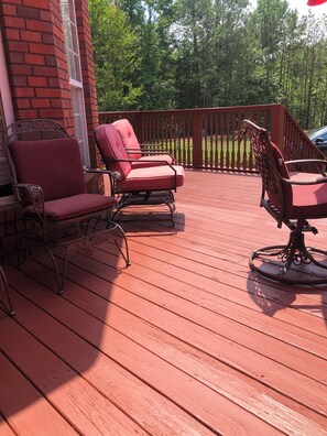 A wooden deck with two red cushioned chairs and a metal table.