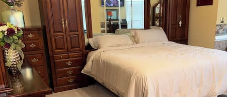 Un dormitorio con una cama grande, un armario de madera, un tocador con espejo y un banco tapizado en rojo.