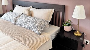 A neatly made bed with patterned pillows, a bedside table with a lamp, a small potted plant, and a painting of a giraffe on a pier.