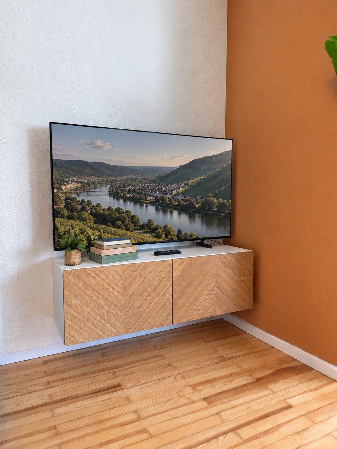 A flat-screen TV mounted on a wooden cabinet with a remote control and books beside it.