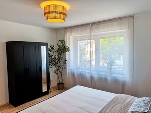 A bedroom with a bed, a window with sheer curtains, a potted plant, and a black wardrobe. - JUPAS° | Saar Home - Nature & Relaxed Vibes (Konz)