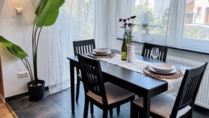 A dining area with a table set for four, surrounded by chairs, with a potted plant and a bottle on the table.