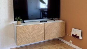 A modern living room with a flat-screen TV mounted on a wooden cabinet, a small potted plant, and a wall-mounted thermostat.