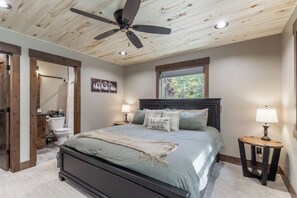 Ein Schlafzimmer mit einem Bett, einem Deckenventilator, einem Fenster und einem Nachttisch mit einer Lampe.