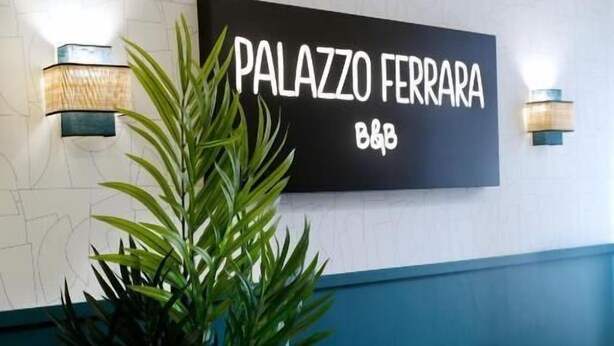 A reception area with a dark sofa, a potted plant, and a wall-mounted sign reading 'PALAZZO FERRARA B&B'. - Palazzo Ferrara  (Naples)
