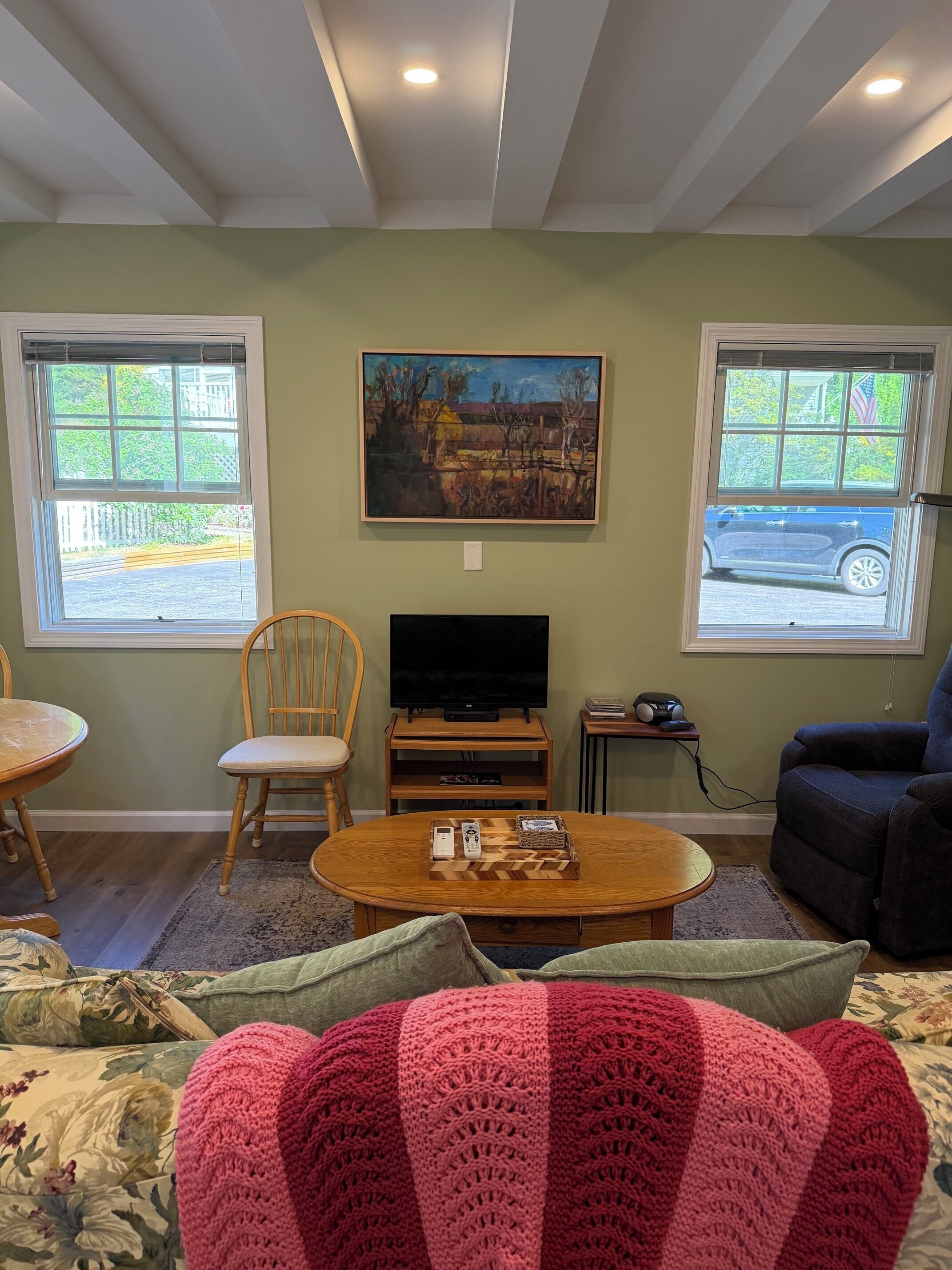 A living room with a television, two windows, a painting, and a cozy seating area.