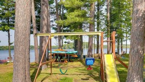 A playground with a swing set, slide, and swing chairs in a wooded area. - Pioneer Paradise - Lakefront home (Conover)