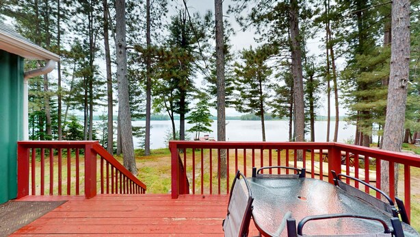 A deck with a metal table and chairs, overlooking a lake with tall trees. - Pioneer Paradise - Lakefront home (Conover)