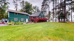 A two-story house with a deck, surrounded by a grassy yard and tall trees. - Pioneer Paradise - Lakefront home (Conover)