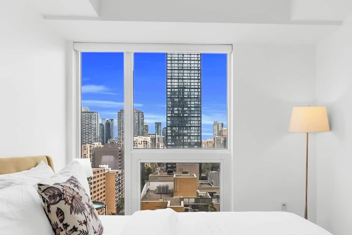 A hotel room with a large bed, a view of the cityscape, and a floor lamp.