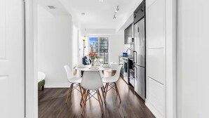 Una cocina moderna con armarios blancos, un comedor con mesa y sillas, y vista a la ciudad a través de una ventana.