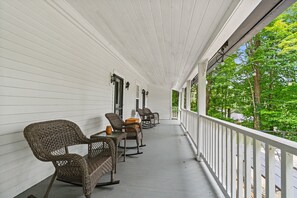 A covered porch with wicker chairs and tables, white siding, and a view of trees. - River House in Fennville (Fennville)