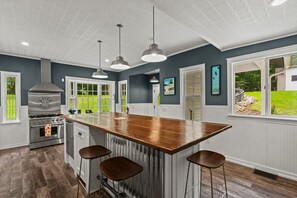 A modern kitchen with a central island, bar stools, a stainless steel range hood, and pendant lighting. - River House in Fennville (Fennville)
