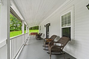 A covered porch with white siding, a rocking chair, a bench, and a table with chairs. - River House in Fennville (Fennville)