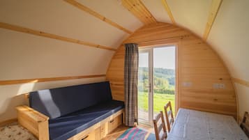 Une pièce chaleureuse avec un plafond en bois, un banc doté d’un coussin foncé, une table recouverte d’une nappe à motifs et une vue sur la verdure à travers une porte vitrée.
